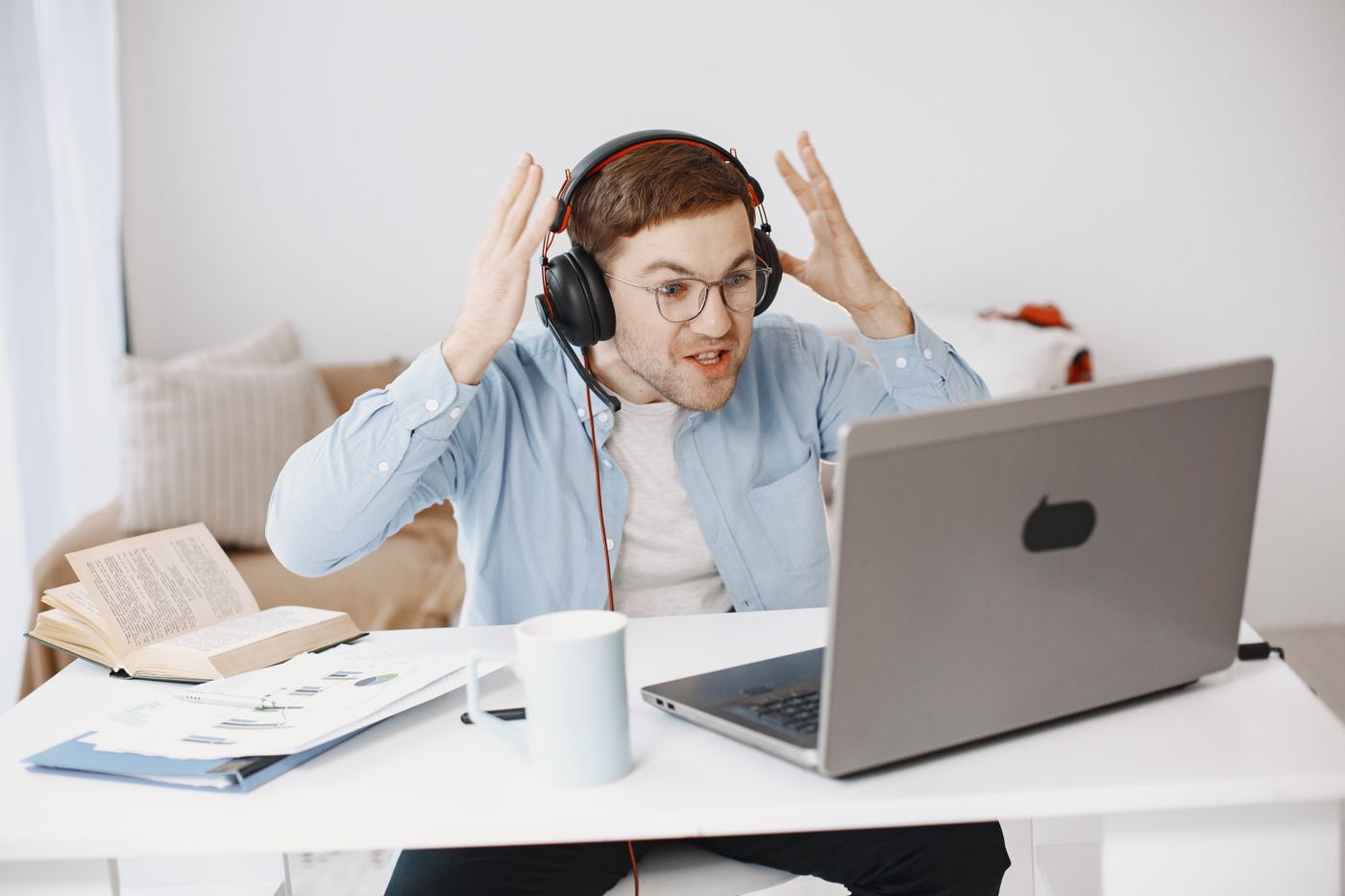 A man in headphones at a home desk reacting with alarm to something that has just appeared on his laptop screen